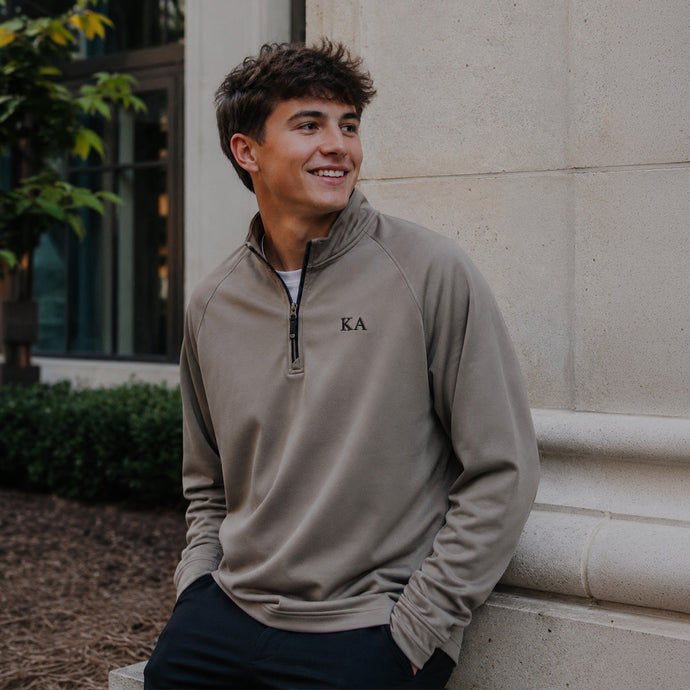 College-aged man wearing the Mushroom Cutter & Buck Adapt quarter-zip with black embroidered Kappa Alpha Order Greek letters outdoors on campus.