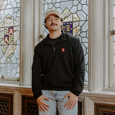 Male model wearing the black Kappa Alpha Order Embroidered Luxe Quarter Zip in front of stained glass windows with fraternity crests.