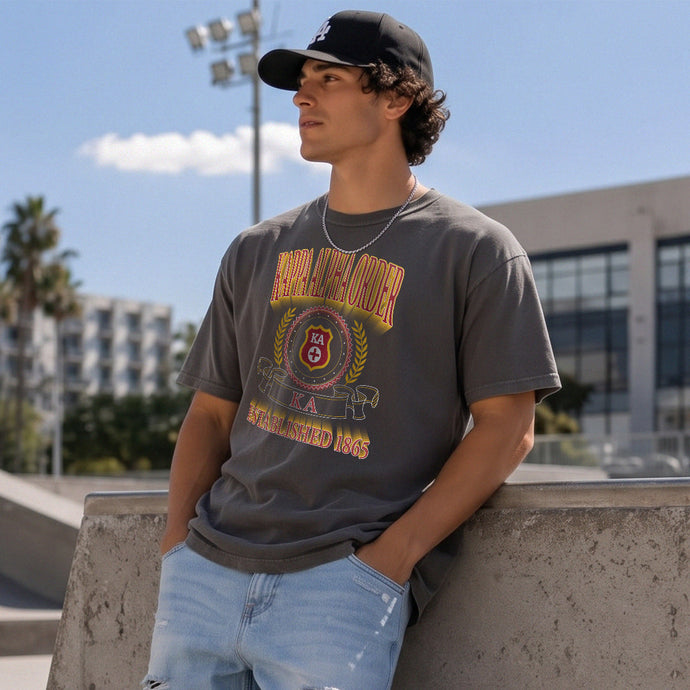 College-aged male wearing the fraternity Collegiate Crest Graphic Tee in charcoal grey, featuring vintage Kappa Alpha Order crest artwork on campus.