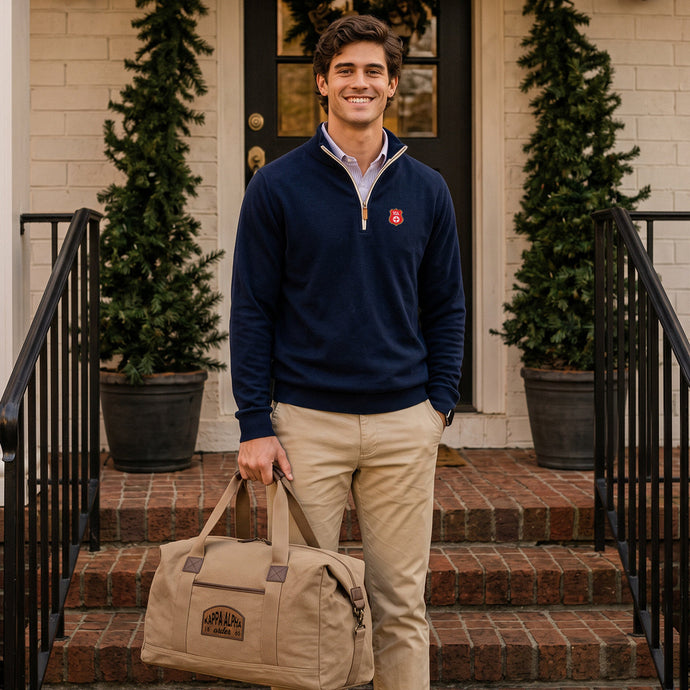 College student wearing fraternity quarterzip holding a tan canvas duffle bag with a leather patch.