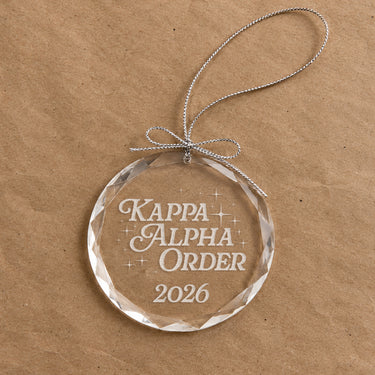 2026 Limited Edition clear glass holiday ornament featuring engraved fraternity design and silver hanging string